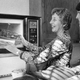 Two women remove a roast from a microwave oven